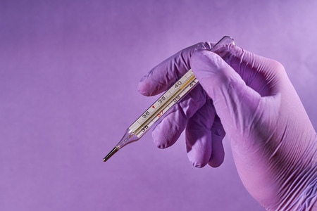 A hand in a medical glove holds a thermometer to measure body temperature.