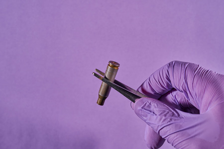 Man's gloved hand with tweezers and bullet casing.の写真素材