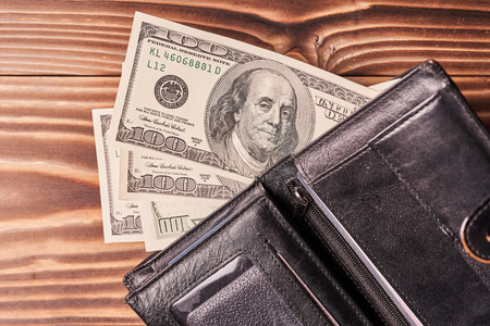 Opened wallet with american dollars on wooden table.