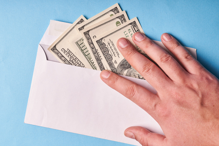 Man's hand holding dollars in an envelope, top view. Blue background.の写真素材