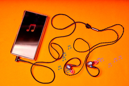 Portable music player on orange background with earphones and wire.