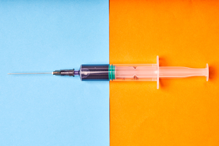 Medical disposable syringe with blue liquid on orange-blue background.の写真素材