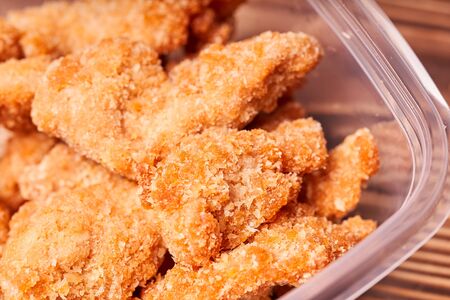 Chicken strips in a plastic container on a wooden table