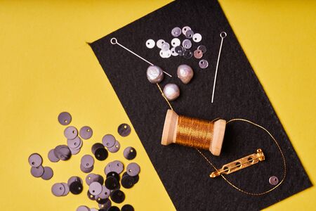 Embroidery products and tools. Coil metal threads, pearls and a pin with the needle on the black...
