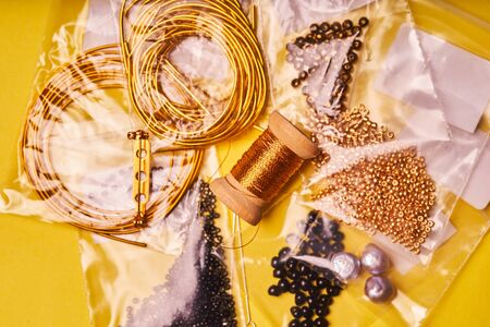 Embroidery products and tools. Coil of metal thread, Japanese beads and sequins with pin and needles on yellow backgroundの写真素材