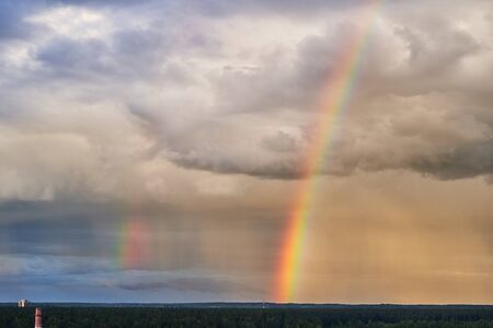 Rainbow over the forest against a contrasting sky. Beautiful scenery.の写真素材