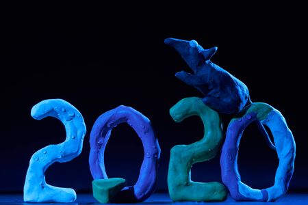 2020 New year design concept. Colored plasticine figures on a black background with mixed light and...