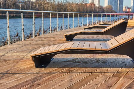 Promenade with railings and wooden sunbeds in the city. Photo composition.