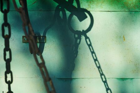 Metal chain with shadow on the wall of green metal panels.