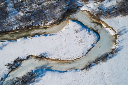 Beautiful Sunny landscape with forest, snow and frozen river. Aerial photography from a drone.