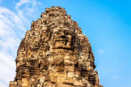 Stone smiling Buddha face on the blue sky background in Angkor Wat temple complex in Cambodia.の写真素材
