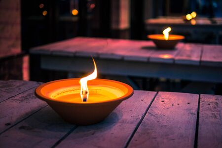 The row of oil lamps flaming at night on the wooden tables, close up. Romantic restarurant exterior.