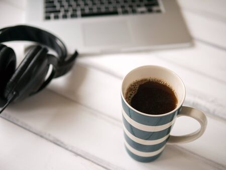 White wooden working desk with notebook, headphones and large mug of coffee.の写真素材