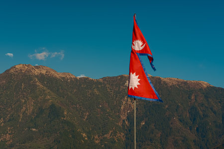 GHOREPANI, NEPAL - JANUARY 9, 2025: Nepal flag against green hills and blue sky with copy space, mountain trekking.の写真素材