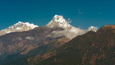 GHOREPANI, NEPAL - JANUARY 9, 2025: Stunning evening views of Annapurna range majestic mountains, lush green hills and snow-capped peaks pan, village with red roofs rustic buildings.の写真素材