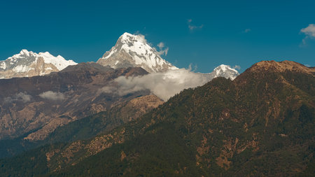 GHOREPANI, NEPAL - JANUARY 9, 2025: Stunning evening views of Annapurna range majestic mountains, lush green hills and snow-capped peaks pan, village with red roofs rustic buildings.の写真素材