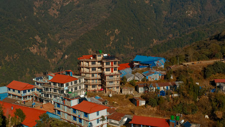GHOREPANI, NEPAL - JANUARY 9, 2025: Stunning evening views of Annapurna range majestic mountains, lush green hills and snow-capped peaks pan, village with red roofs rustic buildings.の写真素材