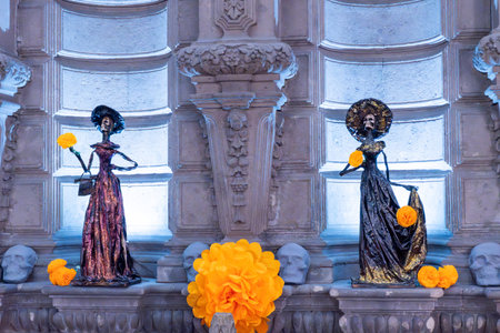 Two statues of women, each holding a flower. One of the statues is wearing a yellow dress. Day of...