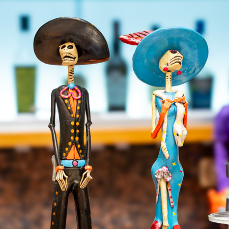 Two skeletons dressed in Mexican garb stand next to each other. One is wearing a hat and the other...