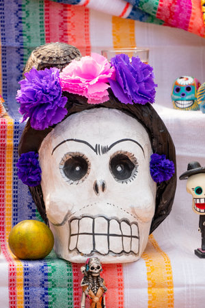 A skull with purple flowers on it, placed on a table with other decorations. The tablecloth is...
