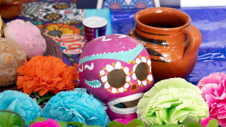 A colorful table with a skull decoration and flowers. The skull is pink and has a smile on it. Day...