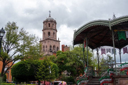 A large building with a tall tower and a green roof. The building is surrounded by trees. Historic...