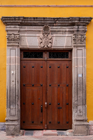 The door is made of wood and has a stone frame. The door is open and the inside is visible. Historic center of Queretaro City, decorations and traditions to celebrate Mexico's Independence Day, colonial architecture, alleys and facadesの写真素材