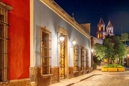 A street with a red building and a blue building. The blue building has a window with a light on it....