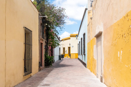 A narrow alleyway with a yellow and blue wall. The alleyway is empty and has a peaceful atmosphere. Historic center of QuerÃ©taro, colonial architecture, decorations for the celebration of Mexico's Independence Day.の写真素材