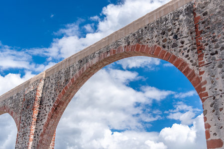 A stone archway with a blue sky in the background. The archway is made of red bricks. Historic center of Querétaro, colonial architecture, decorations for the celebration of Mexico's Independence Day.の写真素材