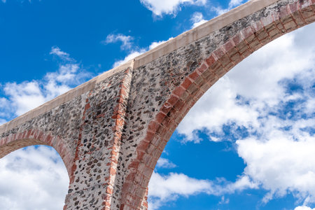 A bridge with a blue sky in the background. The bridge is made of bricks and has a stone arch. Historic center of Queretaro, colonial architecture, decorations for the celebration of Mexico's Independence Day.の写真素材