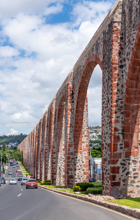 A long stone archway with a red brick wall. The archway is on a street with cars driving by. Historic center of QuerÃ©taro, colonial architecture, decorations for the celebration.の写真素材