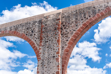 A stone archway with a blue sky in the background. The archway is covered in moss. Historic center of Querétaro, colonial architecture, decorations for the celebration.の写真素材