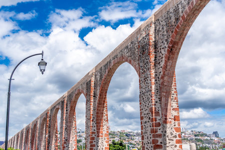 A long, arched bridge made of red bricks and stone stretches across a street. Historic center of Querétaro, colonial architecture, decorations for the celebration.の写真素材