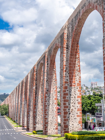 A long, arched stone structure stretches across a street, with a few parked cars visible on the side. Historic center of Querétaro, colonial architecture, decorations for the celebration of Mexico's Independence Day.の写真素材