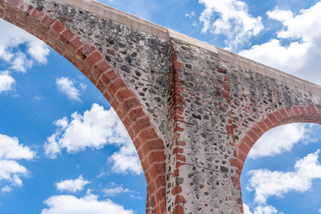 A stone archway with a blue sky in the background. The archway is made of red bricks. Historic center of Queretaro, colonial architecture, decorations for the celebration of Mexico's Independence Day.の写真素材