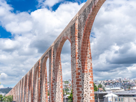 A long brick archway with a cloudy sky in the background. The archway is made of red bricks. Historic center of QuerÃ©taro, colonial architecture, decorations for the celebration of Mexico's Independence Day.の写真素材