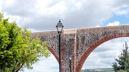 A street lamp is lit up in front of a stone archway. The archway is made of red bricks. Historic center of Queretaro, colonial architecture, decorations for the celebration of Mexico's Independence Day.の写真素材