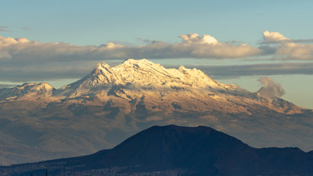 A mountain range with snow on the top and a cloudy sky. The mountains are in the distance and the sky is blue. Panoramic view of Mexico City, snow-covered volcanoes Popocatepetl and Iztaccihuatlの写真素材