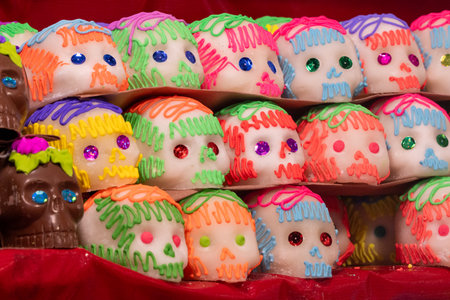 A row of colorful sugar skulls are displayed on a table. The skulls are decorated with frosting. Mexican Day of the Dead tradition, offerings, food, colors, decorations, and papel picado, La Catrina.の写真素材