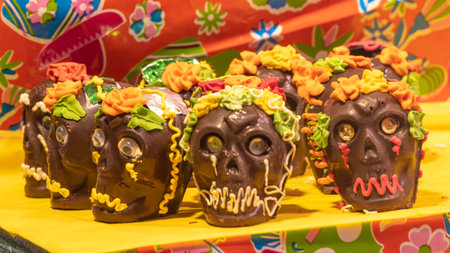 A row of chocolate skulls with flowers on them. The skulls are decorated with frosting. Mexican Day of the Dead tradition, offerings, food, colors, decorations, and papel picado, La Catrina.の写真素材