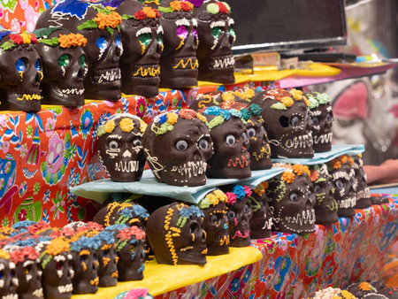 A table full of decorated skulls and flowers. The skulls are decorated with chocolate. Mexican Day of the Dead tradition, offerings, food, colors, decorations, and papel picado, La Catrina.の写真素材