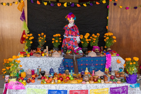 A table with a woman dressed in a costume and a skull on it. The table is covered with fruit. Mexican Day of the Dead tradition, offerings, food, colors, decorations, and papel picado, La Catrina.の写真素材