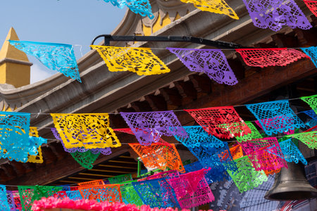 A colorful display of paper flags hangs from a building. The flags are of various colors and sizes. Mexican Day of the Dead tradition, colors, decorations, and papel picado.の写真素材