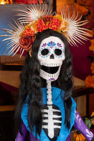 A skeleton with a flower headdress and blue dress. The skeleton is smiling. Mexican Day of the Dead tradition, offerings, food, colors, decorations, and papel picado, La Catrina.の写真素材