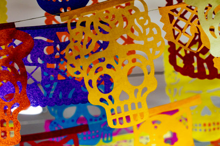 A colorful display of paper skulls and skeletons. The skulls are in various colors and sizes. Mexican Day of the Dead tradition, offerings, food, colors, decorations, and papel picado, La Catrina.の写真素材