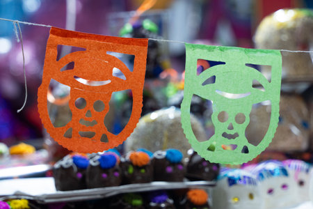 Two paper cutouts of skeletons hang from a string. The skeletons are decorated with hats. Mexican Day of the Dead tradition, offerings, food, colors, decorations, and papel picado, La Catrina.の写真素材