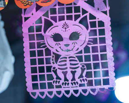A cat skeleton is sitting on a purple paper. The cat is smiling and has a skeleton face. Mexican Day of the Dead tradition, offerings, food, colors, decorations, and papel picado.の写真素材
