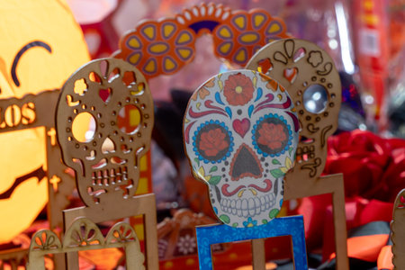 A skull is sitting on a table with other skulls and a pumpkin. The skulls are decorated with flowers. Mexican Day of the Dead tradition, offerings, food, colors, decorations, and papel picado, La Catrina.の写真素材