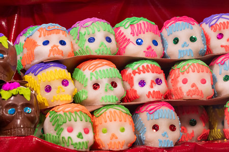 A display of colorful sugar skulls with various shades of green, red, and blue icing. Mexican Day of the Dead tradition, offerings, food, colors, decorations, and papel picado.の写真素材